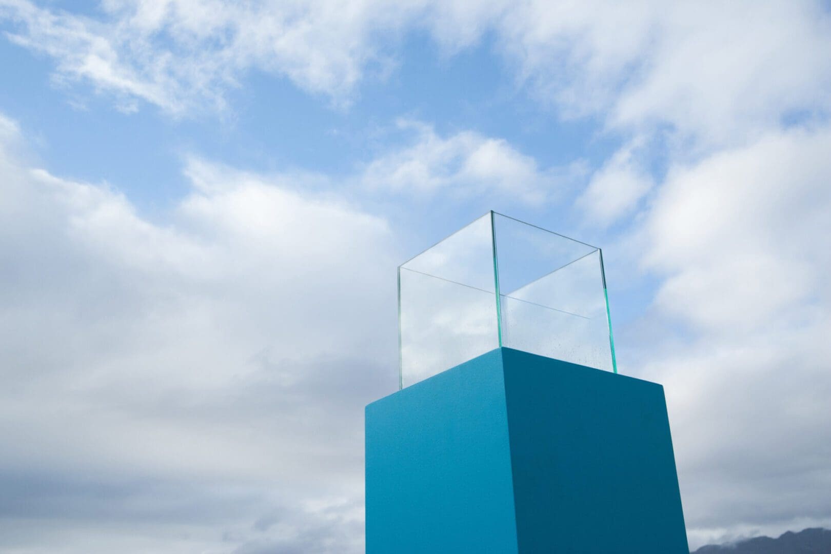 Glass cube on blue pedestal under sky